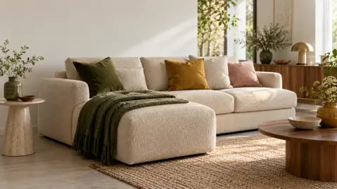 En lys sofa med sjeselong og et mosegrønt pledd, sett på skrå i en lys stue